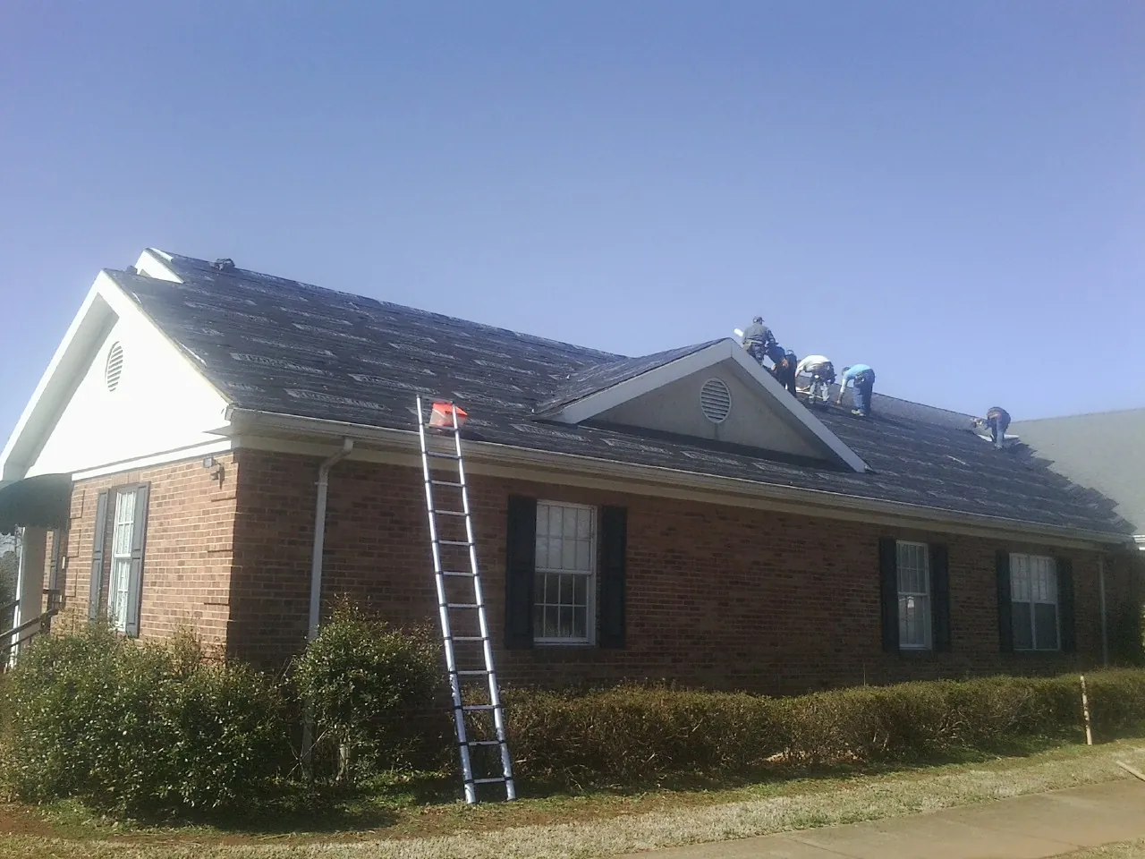 Crew tearing shingles off a brick ranch roof with a ladder set in Garden City