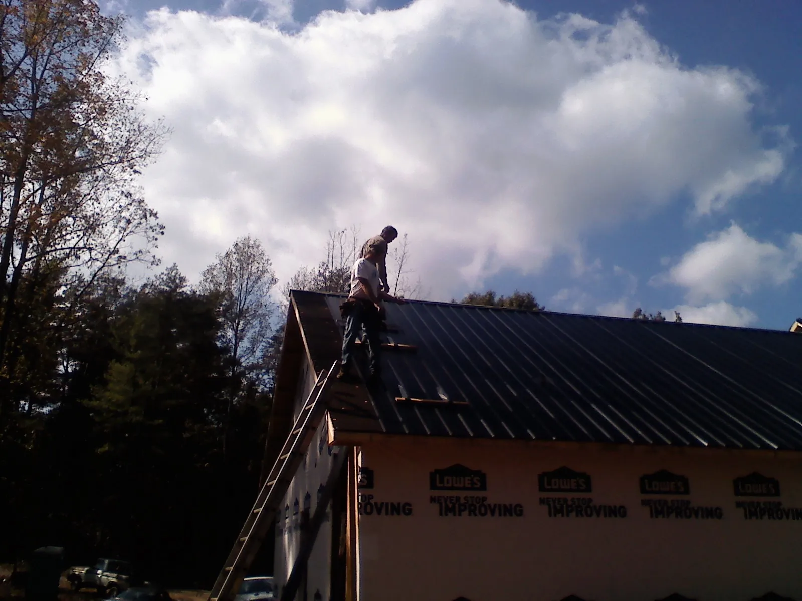 Roofer fastening dark metal panels high against a cloudy sky, from a Roof Inspection job in Garden City